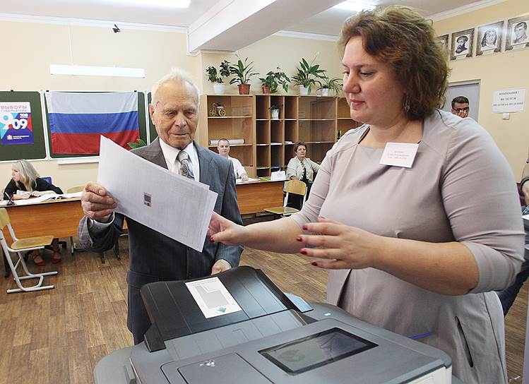 Член участковой избирательной комиссии помогает нижегородцу внести бюллетень в электронную урну