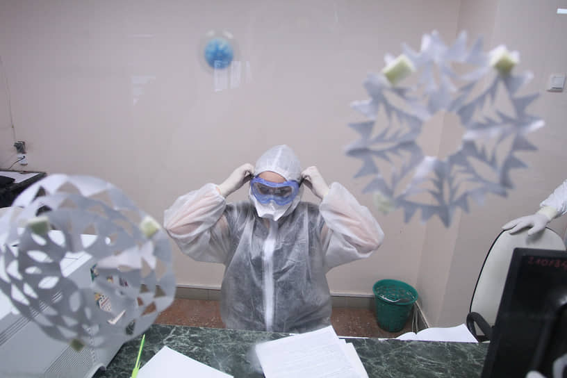Снежинки на окне регистратуры на фоне врача в защитном костюме сейчас больше напоминают коронавирус