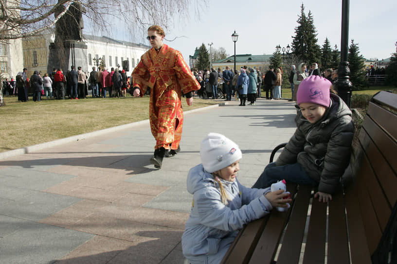 Священнослужитель проходит мимо детей, играющих на скамейке у храма Михаила Архангела