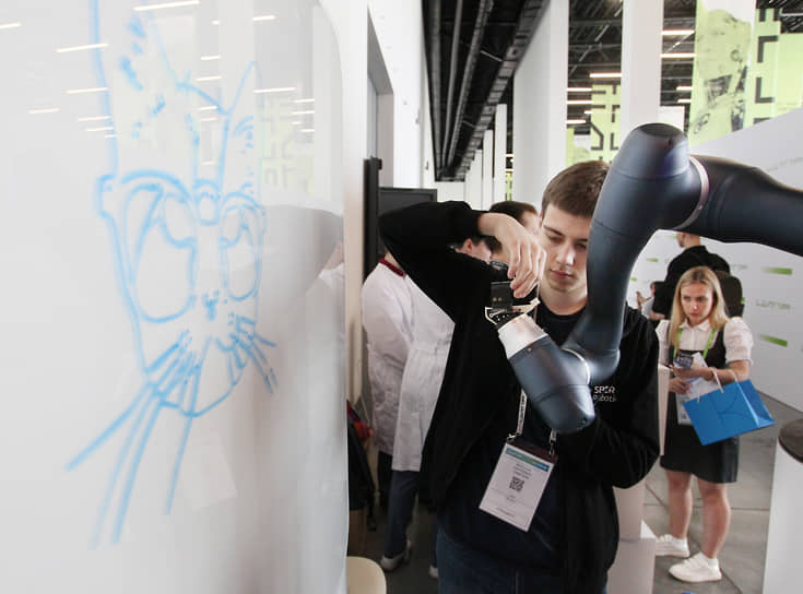 Молодой участник выставки настраивает печатающую головку робота для рисования