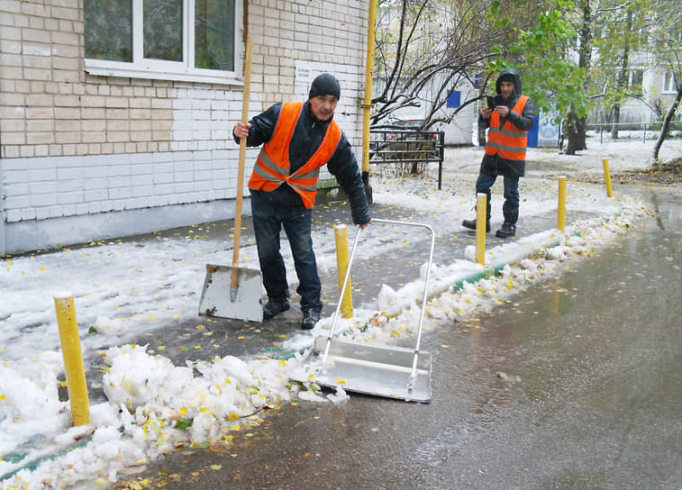 Дворники сгребают выпавший снег с тротуара