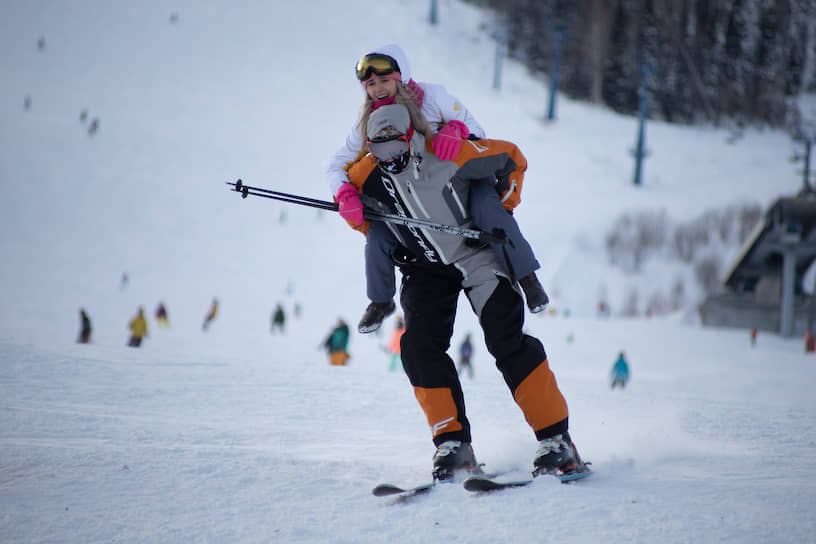 Лыжник спускается с пассажиром на плечах по горнолыжной трассе на горе Зеленая в Шерегеше