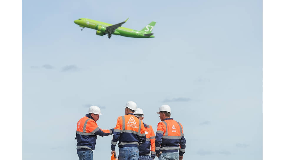Самолет авиакомпании S7 Airlines взлетает на фоне рабочих компании ОАО «Новосибирскавтодор» во время работ по реконструкции взлётно-посадочной полосы в аэропорту «Толмачево» в Новосибирске