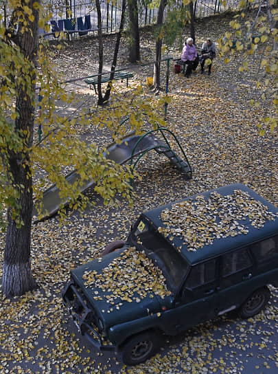 Автомобиль, засыпанный осенней листвой, на аллее парка в Омске