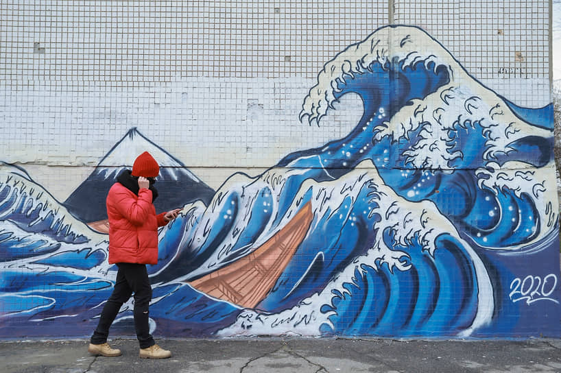 Власти Новосибирской области продлили режим повышенной готовности из-за угрозы распространения коронавирусной инфекции до конца текущего года. Прохожий в маске идет на фоне граффити на стене по мотивам гравюры «Большая волна в Канагаве» японского художника Кацусики Хокусая