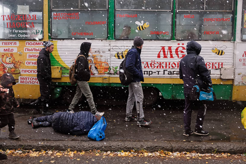 Пассажиры перед посадкой в автобус обходят лежащего на асфальте мужчину в Прокопьевске 