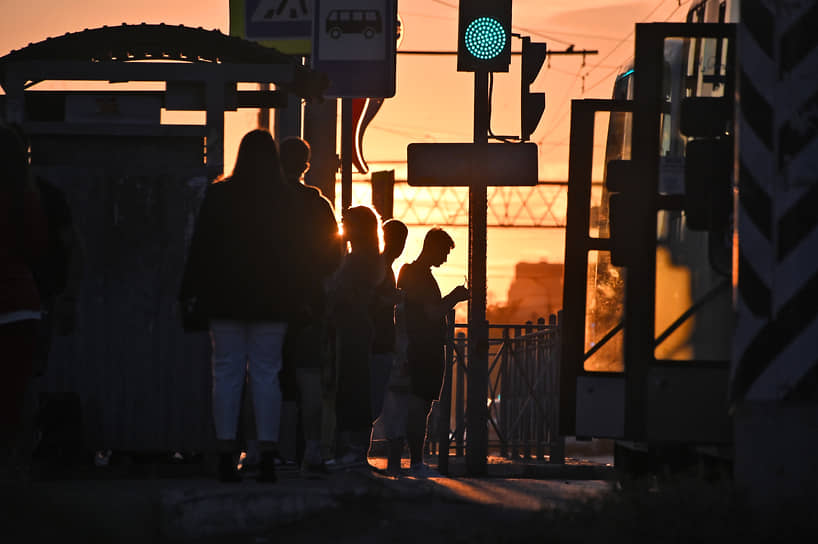 Люди стоят на остановке общественного транспорта на закате в Омске