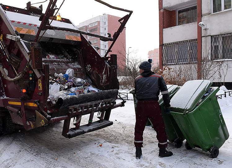Сотрудник компании по вывозу мусора во время загрузки контейнеров с отходами