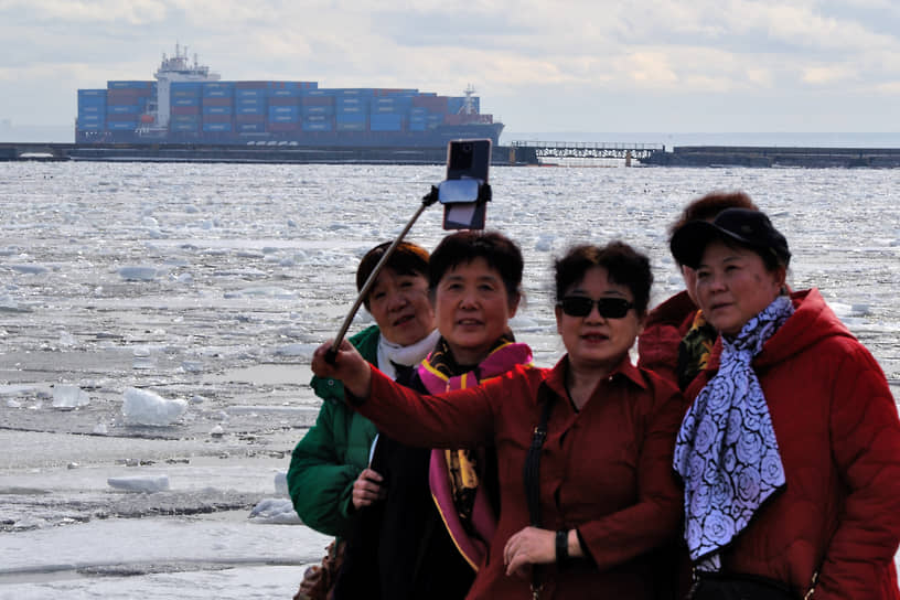 Иностранные туристы фотографируются на фоне севшего на мель контейнеровоза
