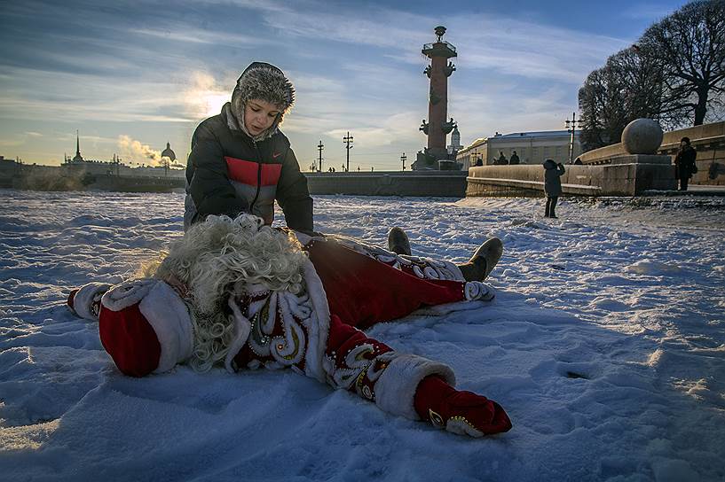 Мужчина в костюме Деда Мороза играет с мальчиком на льду реки Невы в районе Стрелки Васильевского острова