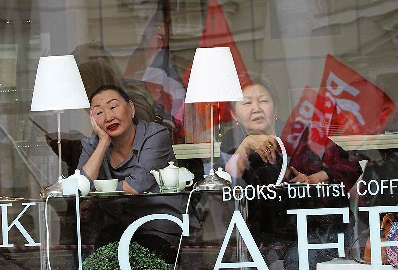 Посетители кафе смотрят в окно на участников праздничного шествия, посвященного Дню международной солидарности трудящихся