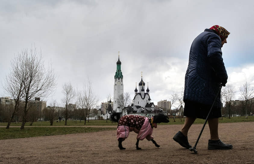 Пожилая женщина гуляет с собакой в парке Строителей 