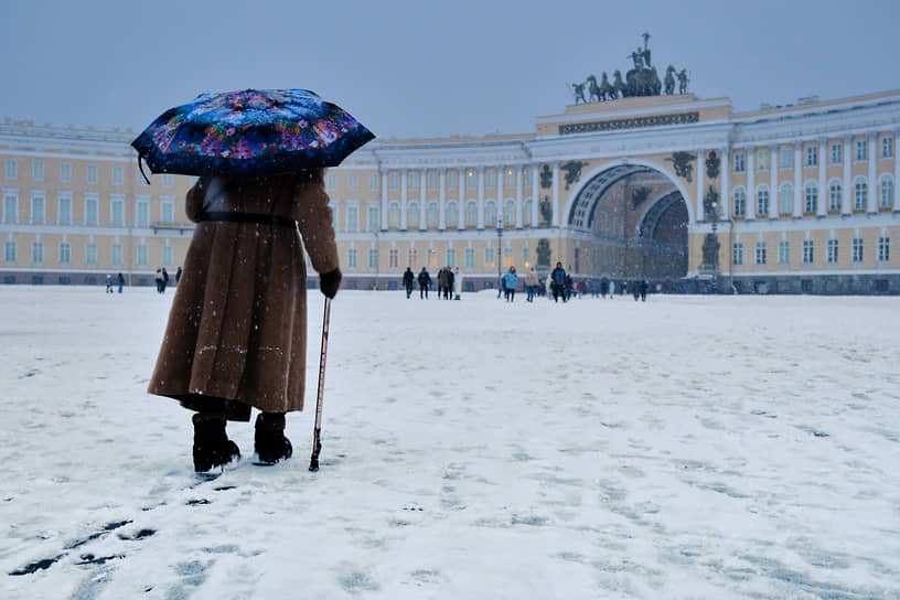 Пожилая женщина под зонтом идет по Дворцовой площади