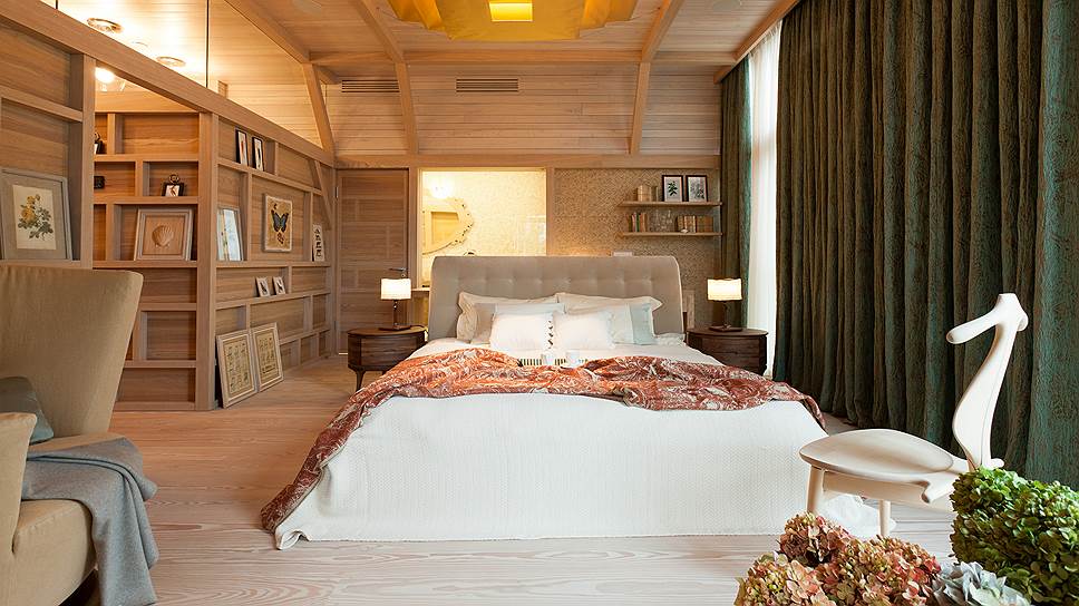 В спальне стены оформлены бежево-розовыми обоями, а панорамное окно драпировано плотными шторами из ажурной ткани