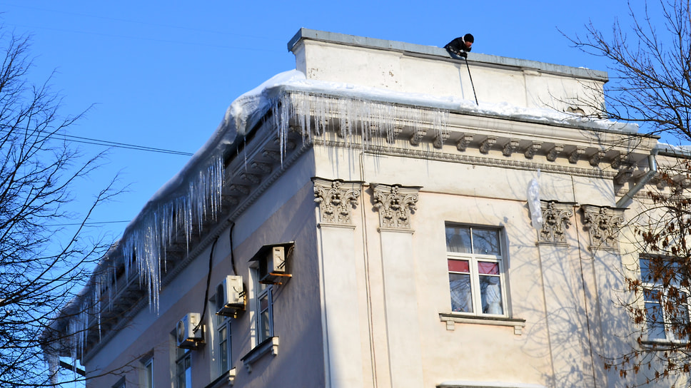 Мужчина сбивает сосульки с крыши административного здания