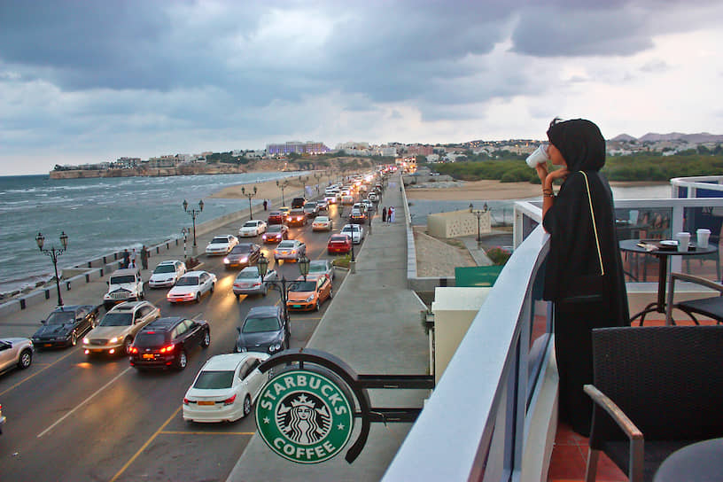 Женщина в кофейне Starbucks в Мускате смотрит на море