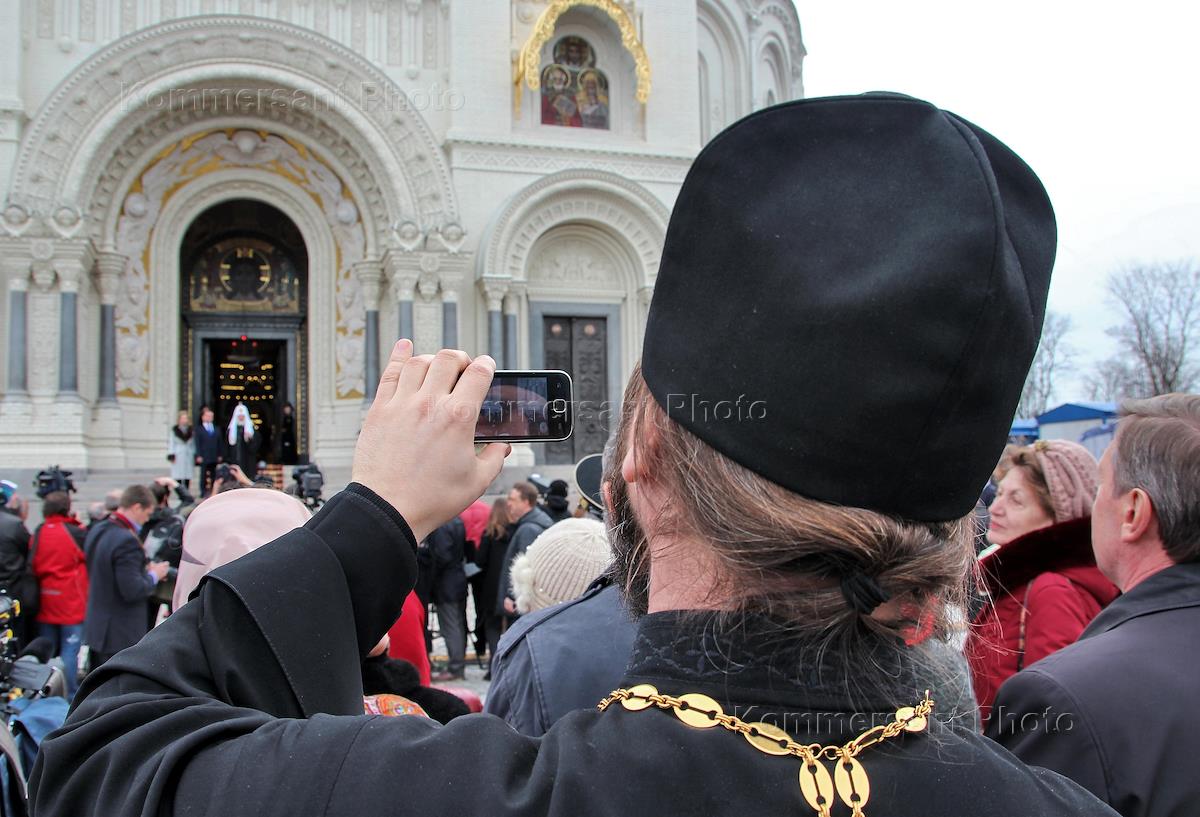 Религии петербурга. Либералы в церкви. Священник фотографируется у стены.